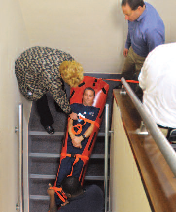 Under the watchful eyes of staff members and Nick Gabriele, upper right, an exercise controller with Russell Phillips and Associates, Backus Paramedic Michael De-Bernardo is lowered down a stairwell on a special patient transport sled as part of an evacuation drill that took place at Backus Monday.